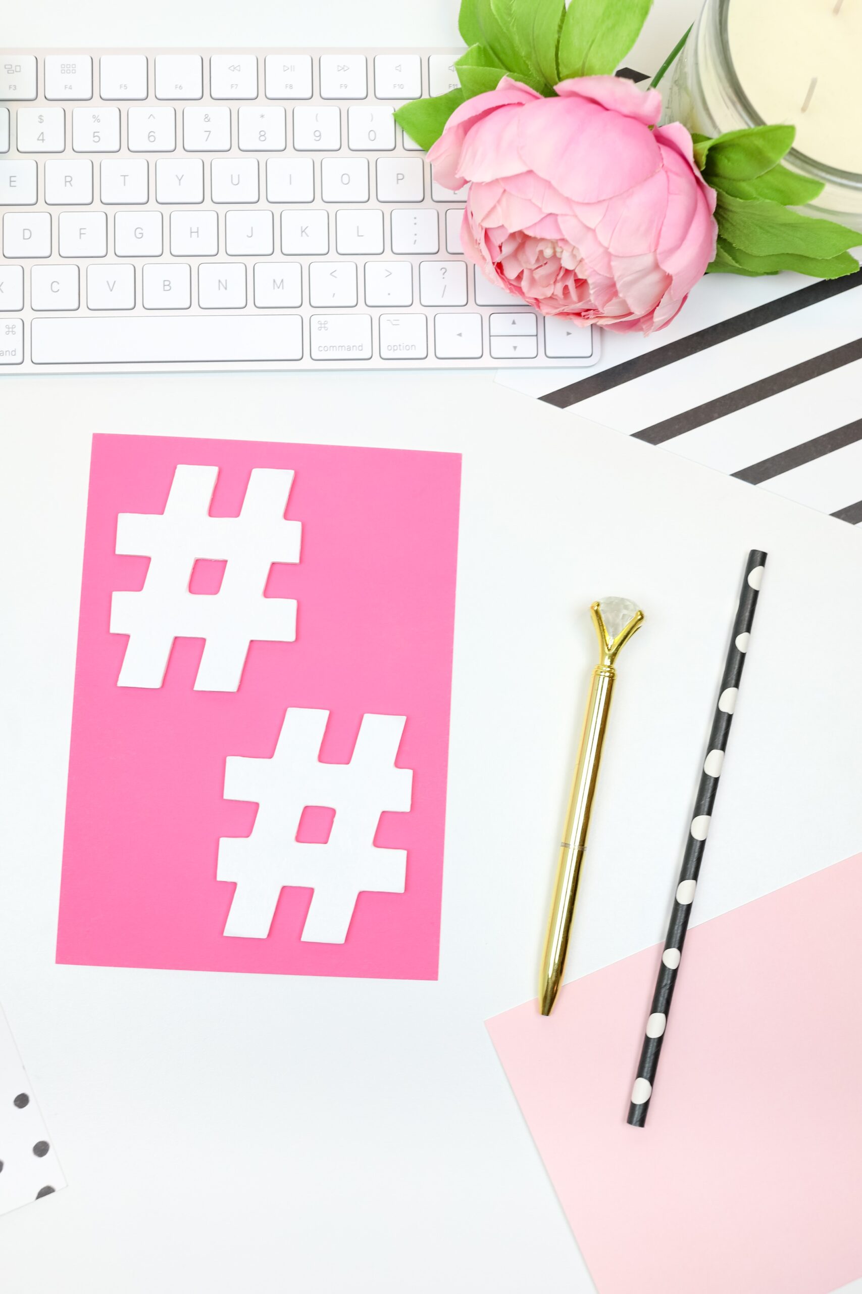 close up of a social media manager's desk with pink notebook and hot pink poster with social media hashtags on it. This is the featured image for a post about why female business owners should hire a social media manager